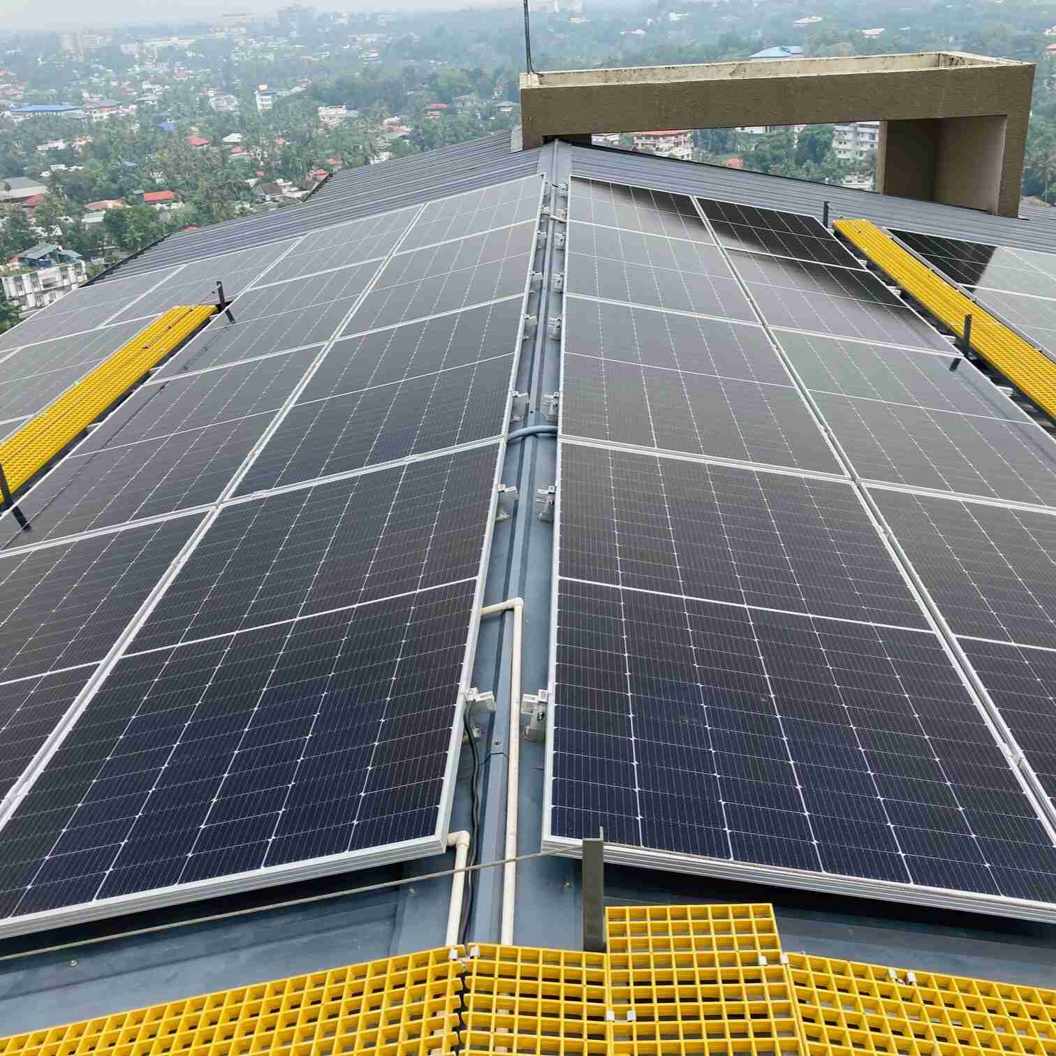 Rooftop solar panels glistening under soft light, with yellow walkways for maintenance. Overlooks a lush, foggy cityscape below, conveying innovation.